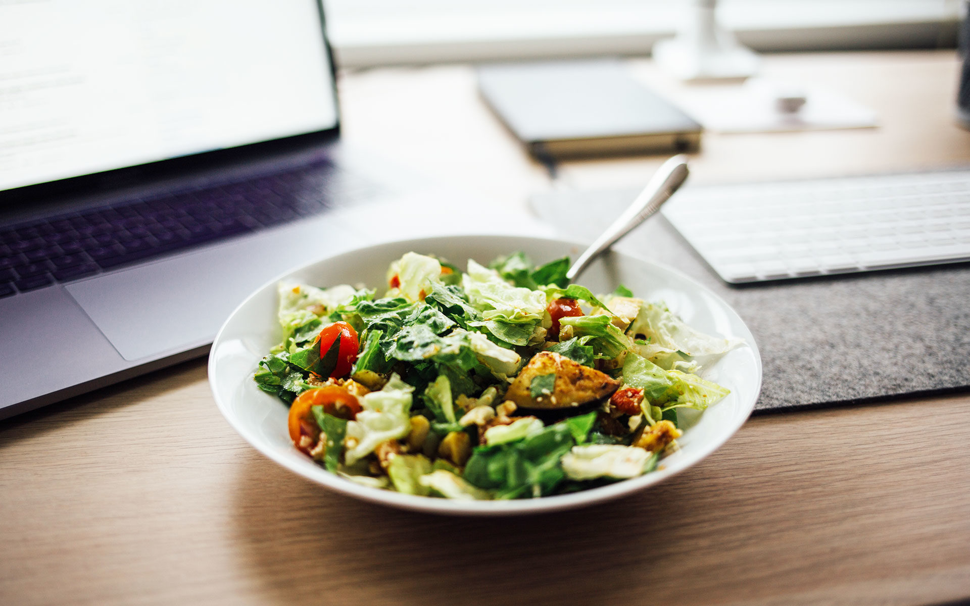 a bowl of salad on a desk in front of a laptop