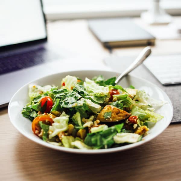 a bowl of salad on a desk in front of a laptop