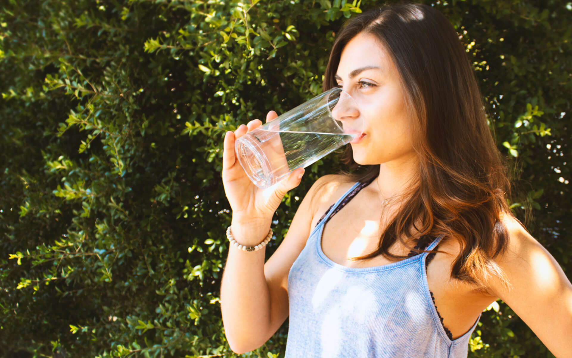 woman with dark hair drinking a glass of water