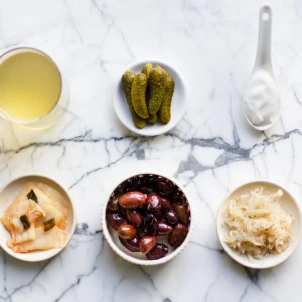 vinegar, pickles, yogurt, kimchi, olives and sauerkraut in bowls on a marble table