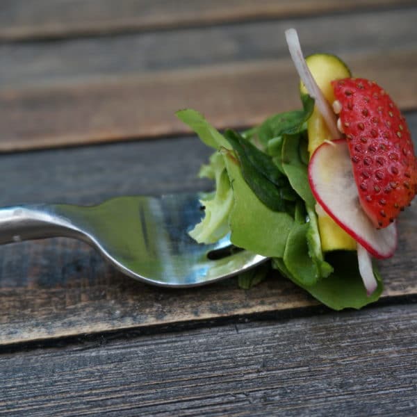 a fork holding lettuce, a radish and strawberry.