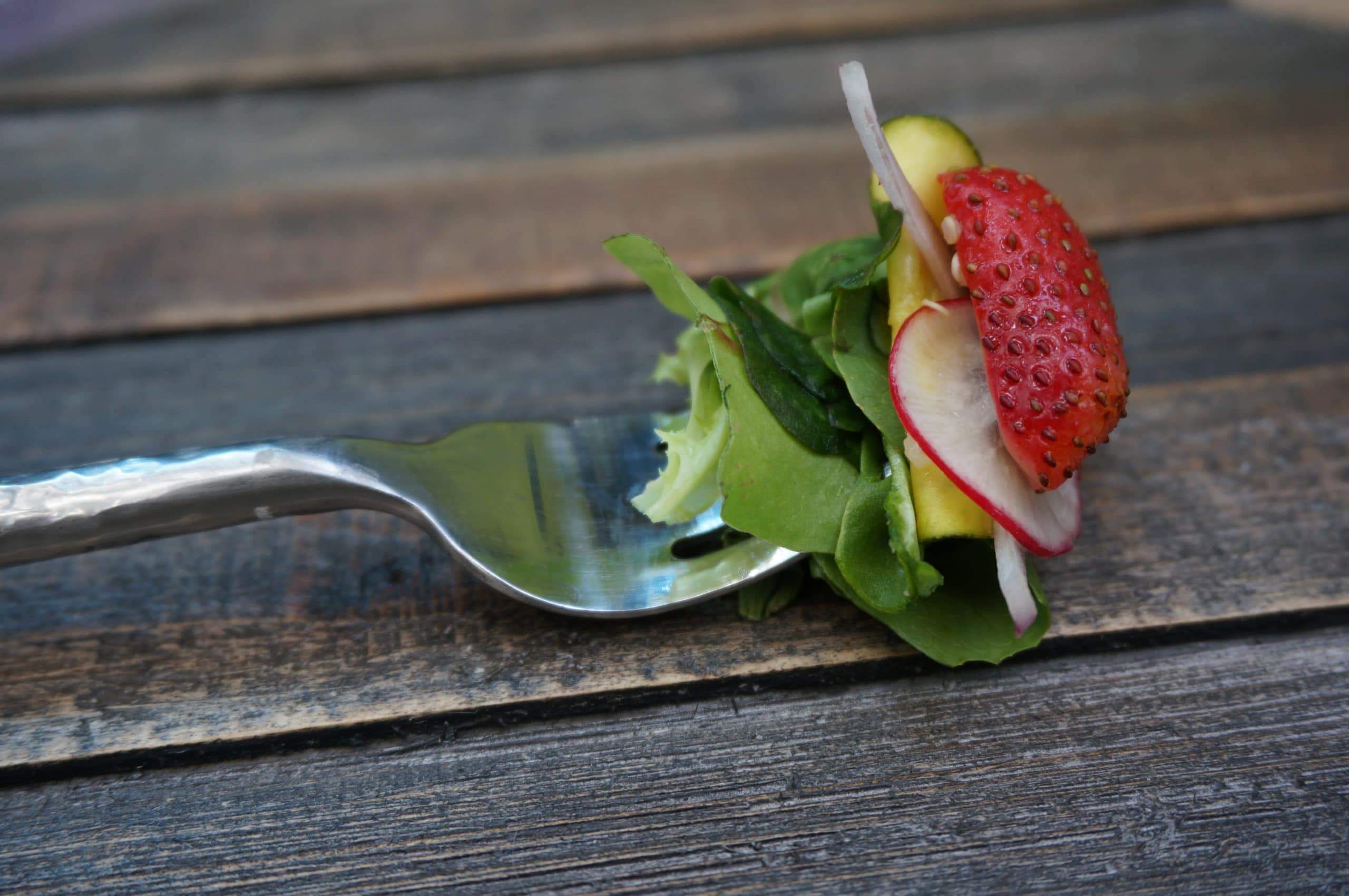 a fork holding lettuce, a radish and strawberry.