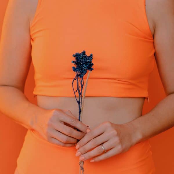 Person wearing an orange outfit and holding a flower in front of an orange background