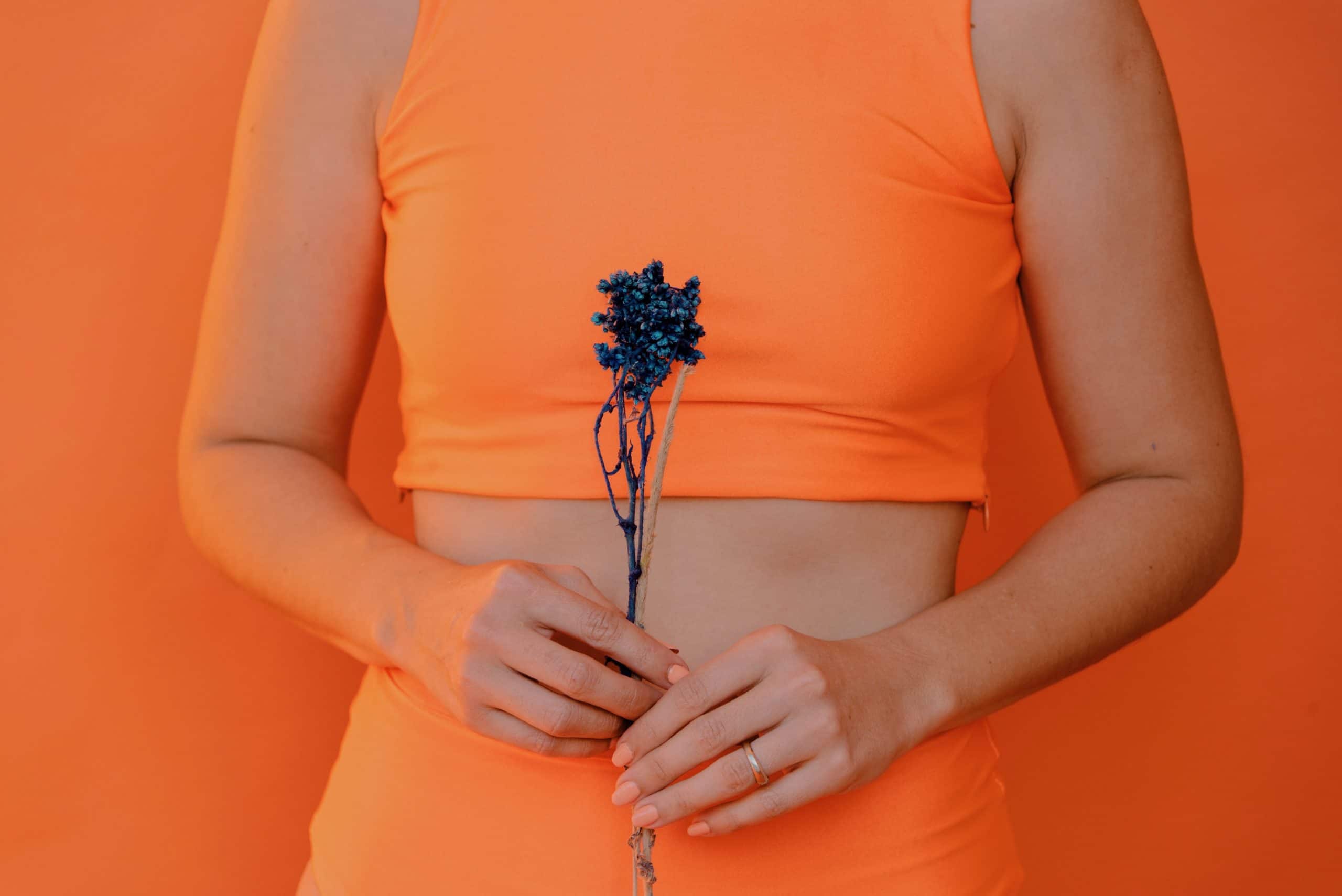 Person wearing an orange outfit and holding a flower in front of an orange background