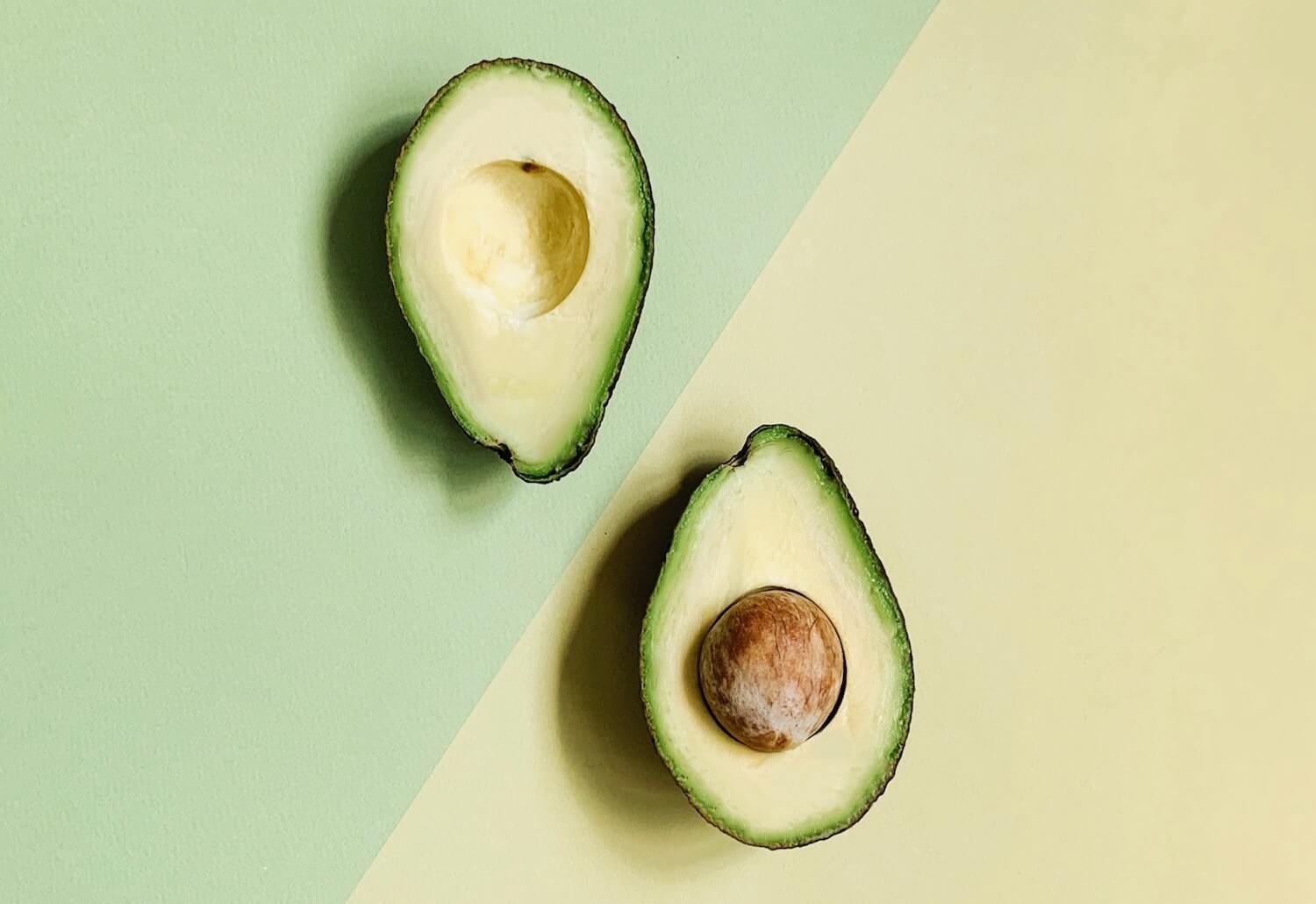 Two halves of an avocado on a yellow and green background