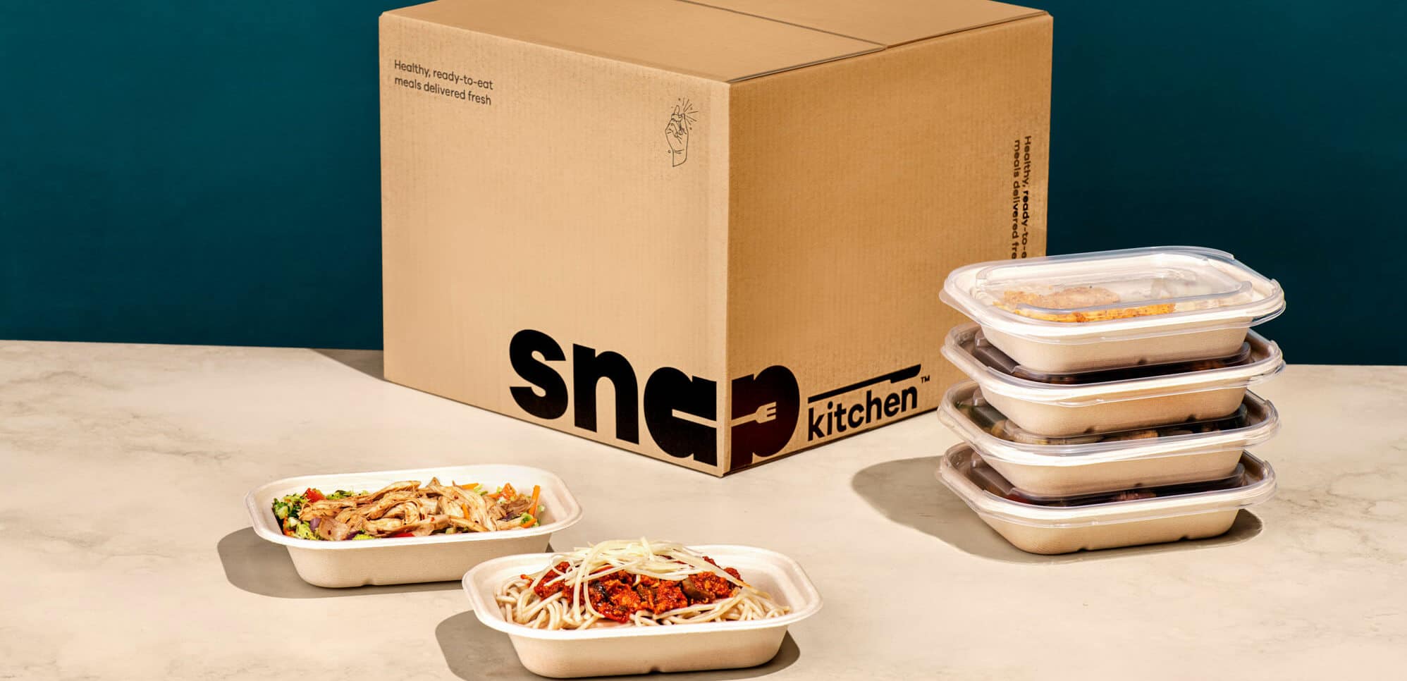 Cardboard Snap Kitchen box with a stack of packaged meals next to it