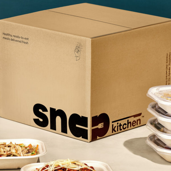 Cardboard box with the Snap Kitchen logo, and 4 prepped meals in containers stacked next to it. In the foreground is an open container with chicken and vegetables