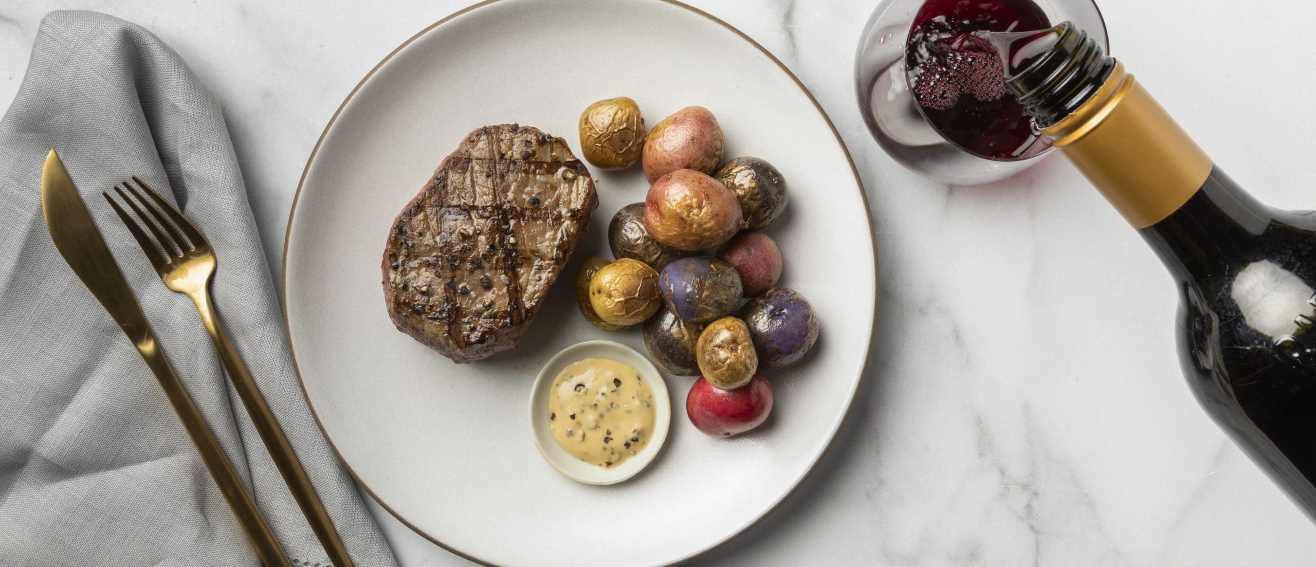 Mini roasted potatoes and steak on a plate with a glass of red wine
