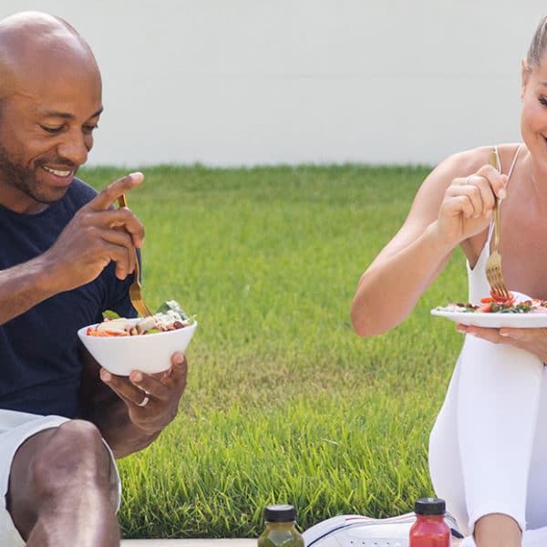 A man and a woman sit together on the grass eating