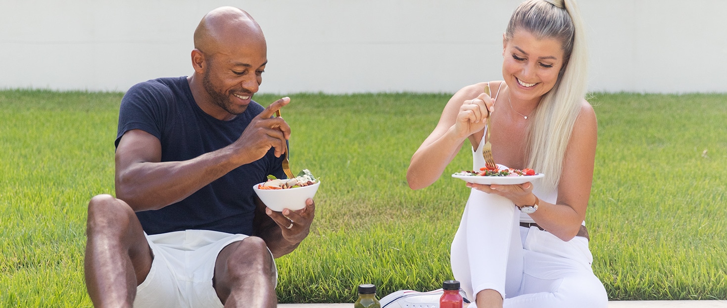 A man and a woman sit together on the grass eating