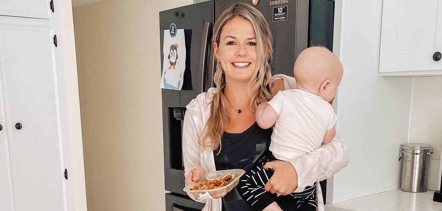 Mom with a baby in her kitchen, holding a Snap Kitchen meal