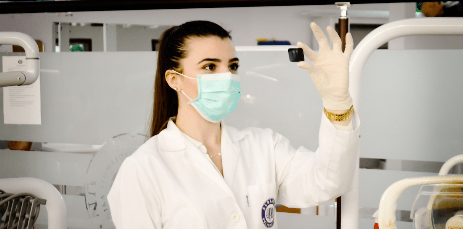 Female scientist wearing a surgical mask, white coat and latex gloves in a laboratory setting