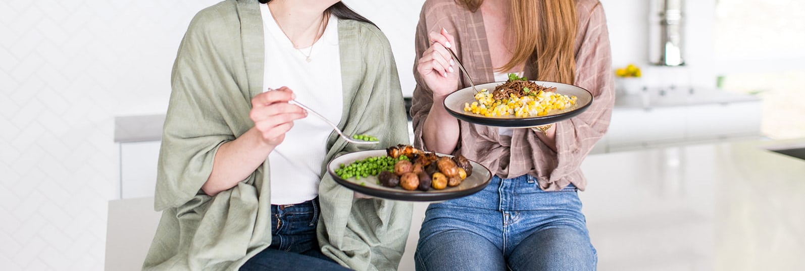 Two people eating food off of plates in front of a white background