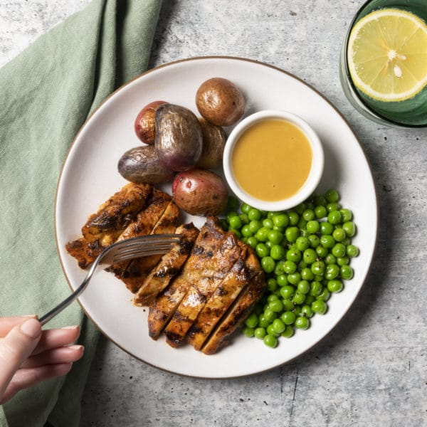 Plate of roasted chicken, red potatoes, peas and gravy with a glass of water on the side
