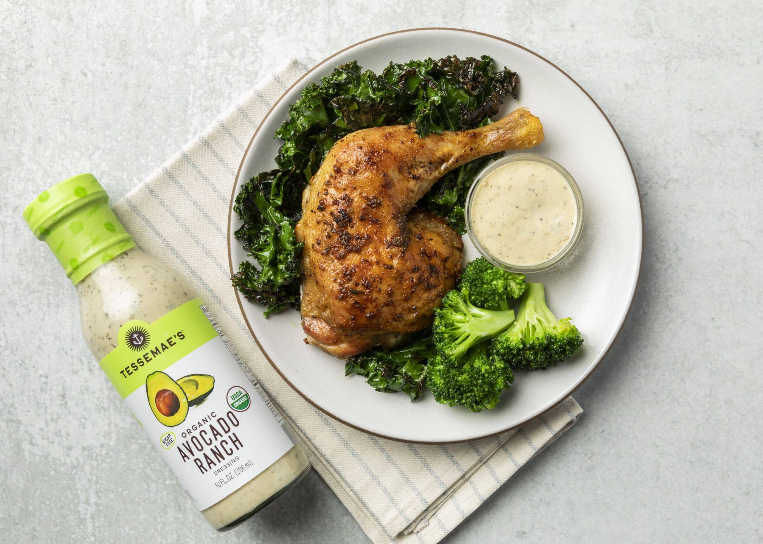 Rotisserie chicken thigh on a bed of greens with Tessamae's Avocado Ranch dressing on the side