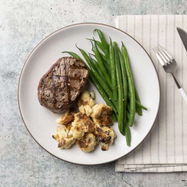 Steak with turnip mash and green beans on a white plate with silverware