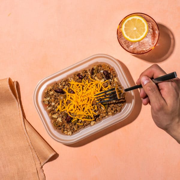 Bison quinoa bowl on a light pink background with a glass of water and someone's hand holding a fork