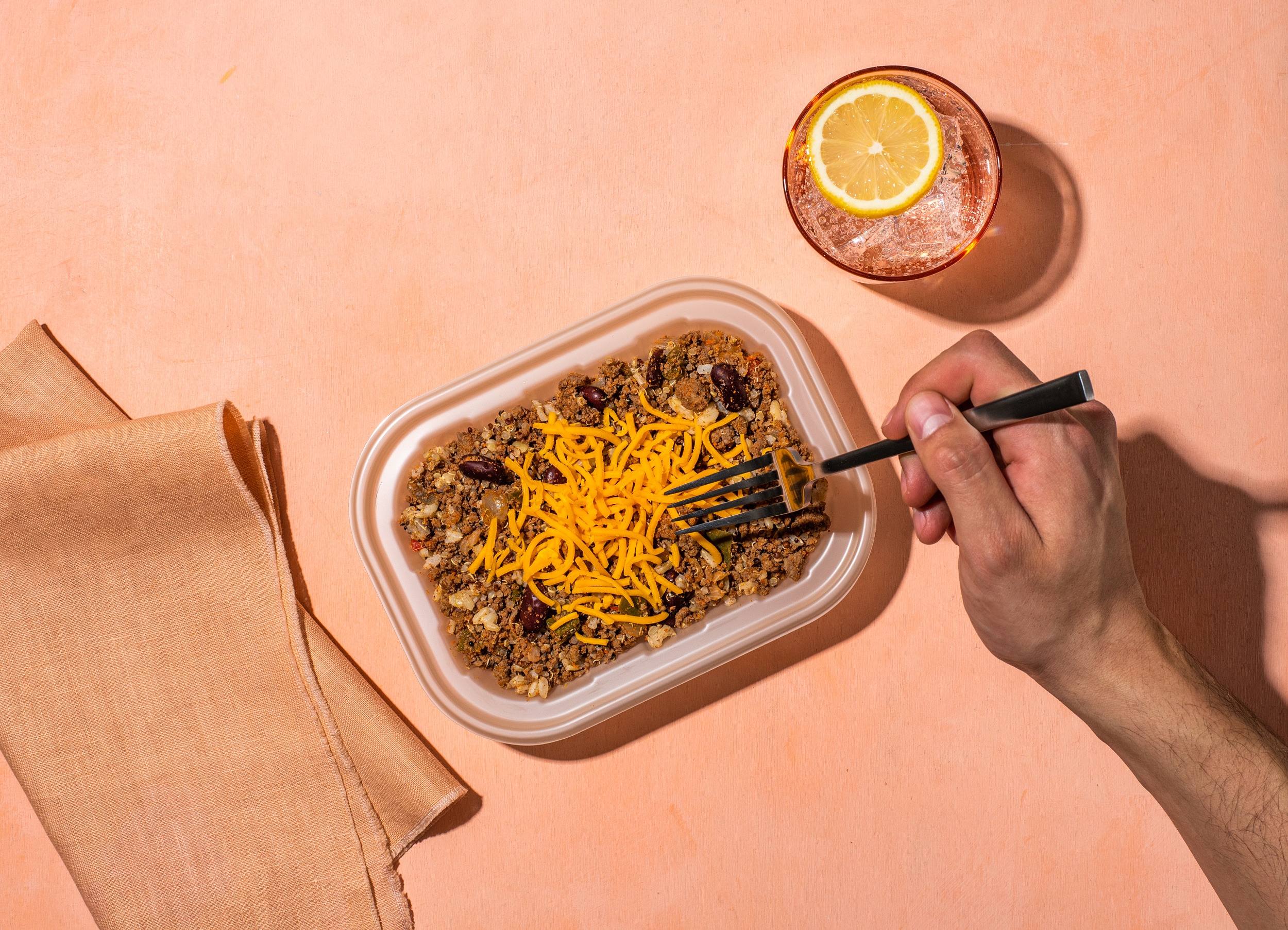Bison quinoa bowl on a light pink background with a glass of water and someone's hand holding a fork