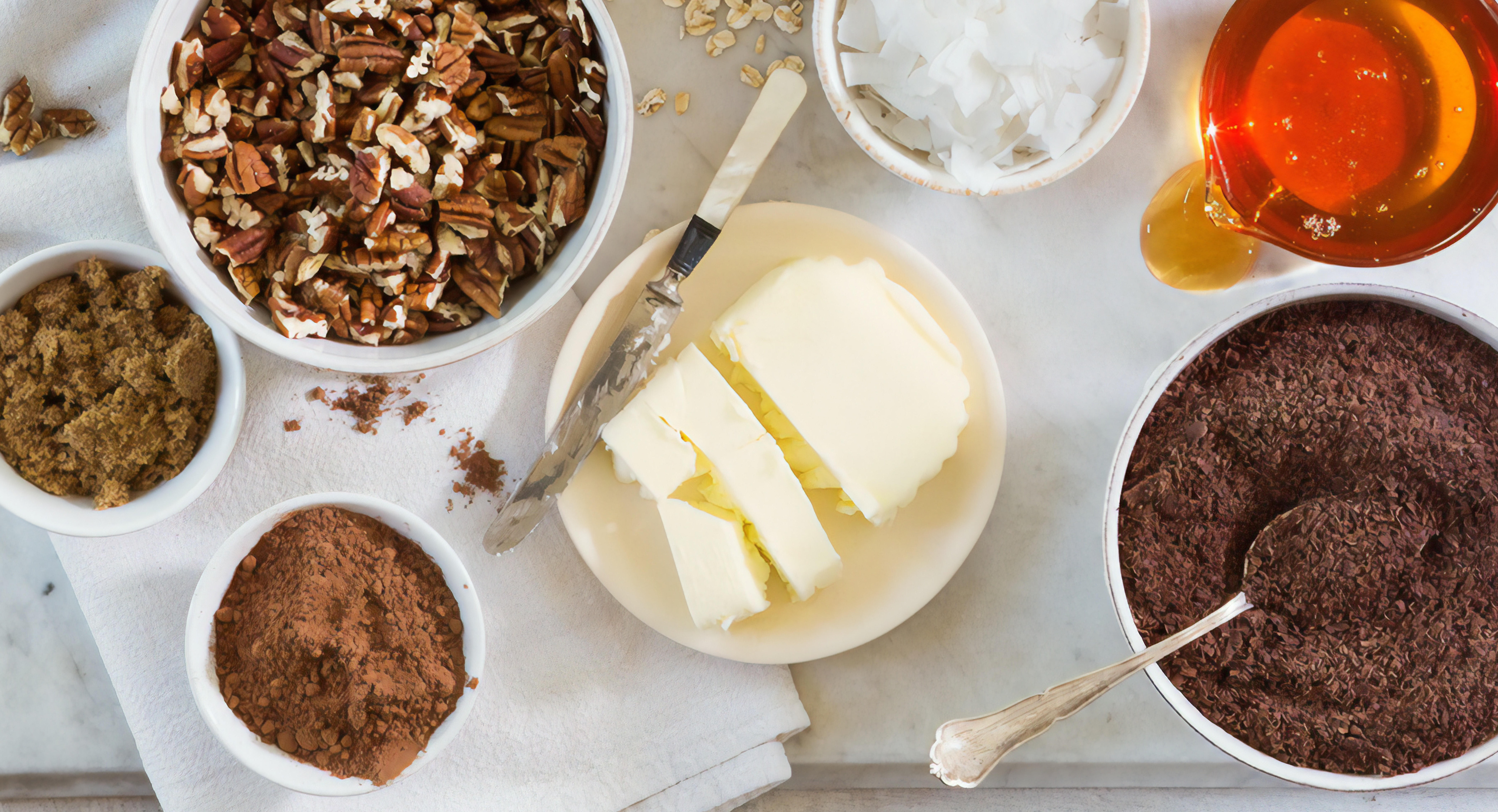 Ingredient bowls with butter, coconut, honey, chocolate flakes, walnuts, cocoa powder, and brown sugar