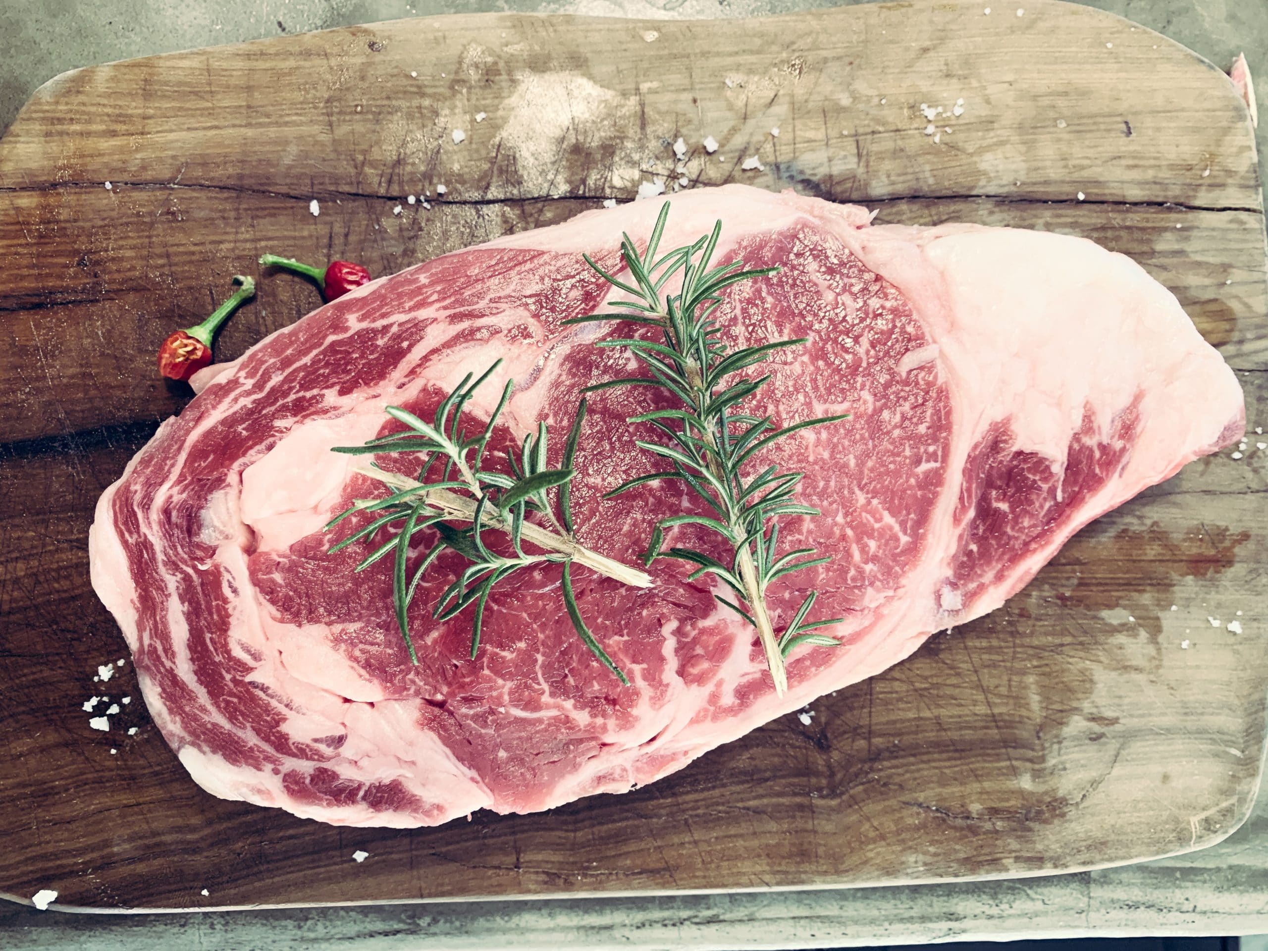 Raw slab of steak with sprigs of thyme on top of a rustic wood board