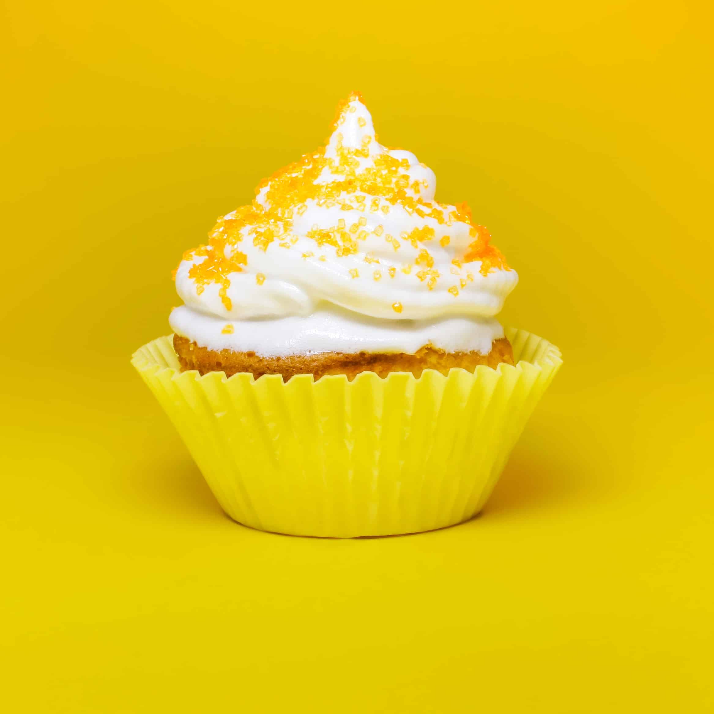 Cupcake with white frosting and lemon in a yellow wrapper on a bright yellow background