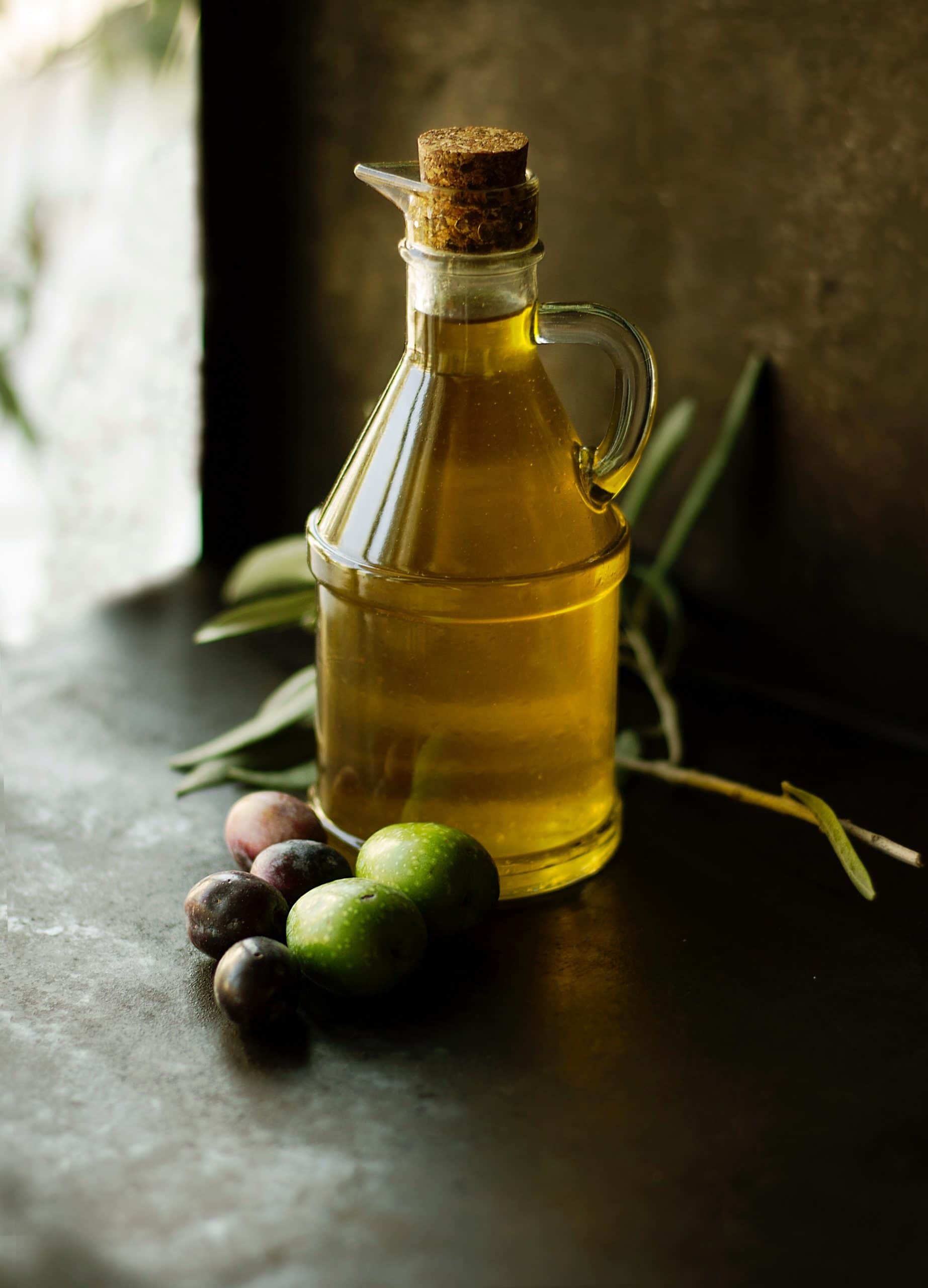 Jar of olive oil on a dark countertop with green and black olives