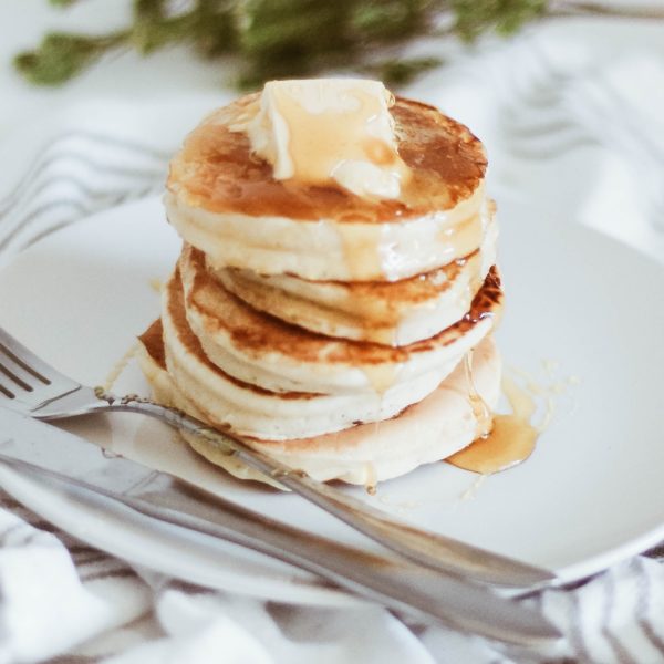 Stack of small fluffy pancakes with syrup and a chunk of butter on top