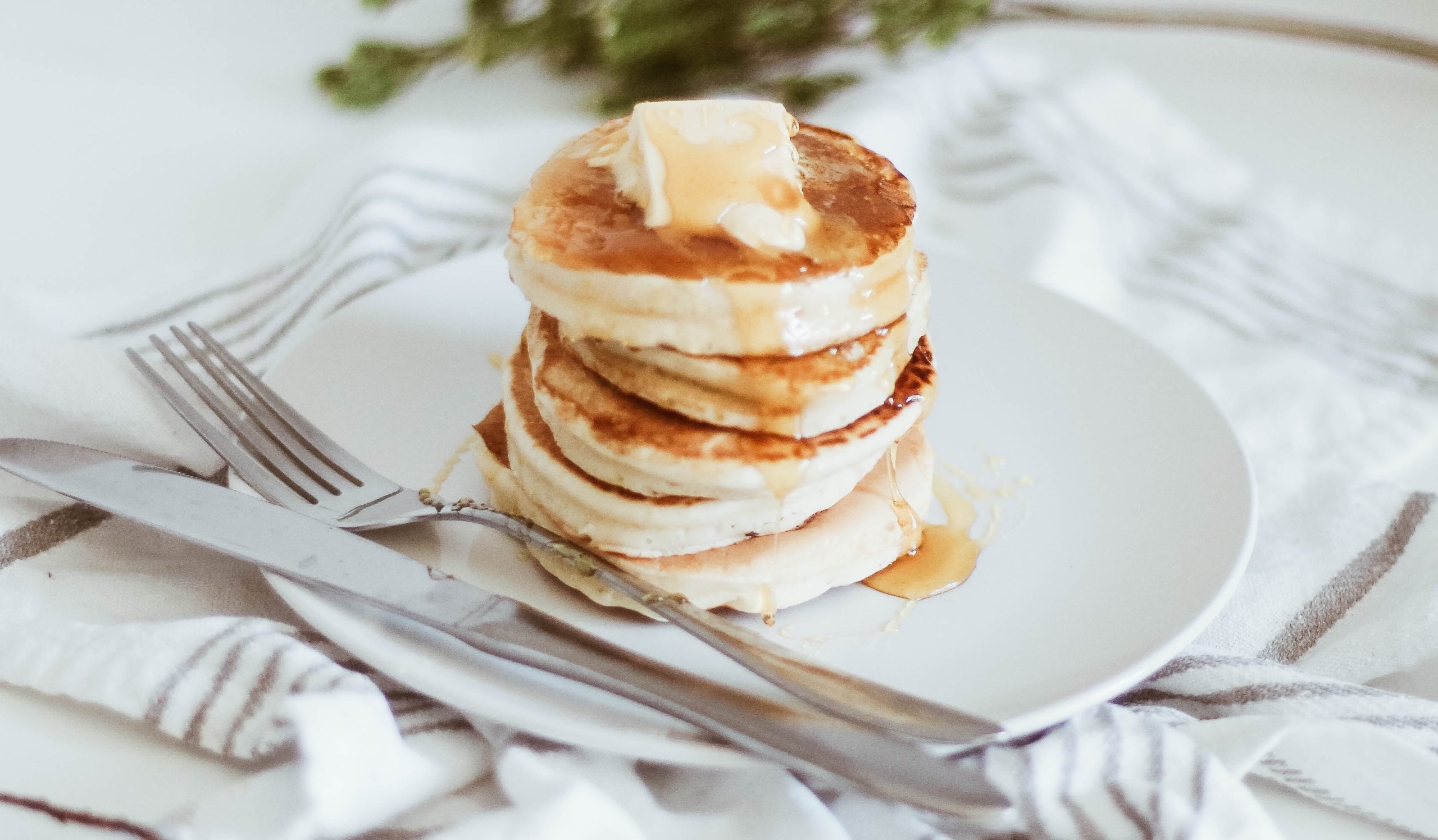 Stack of small fluffy pancakes with syrup and a chunk of butter on top