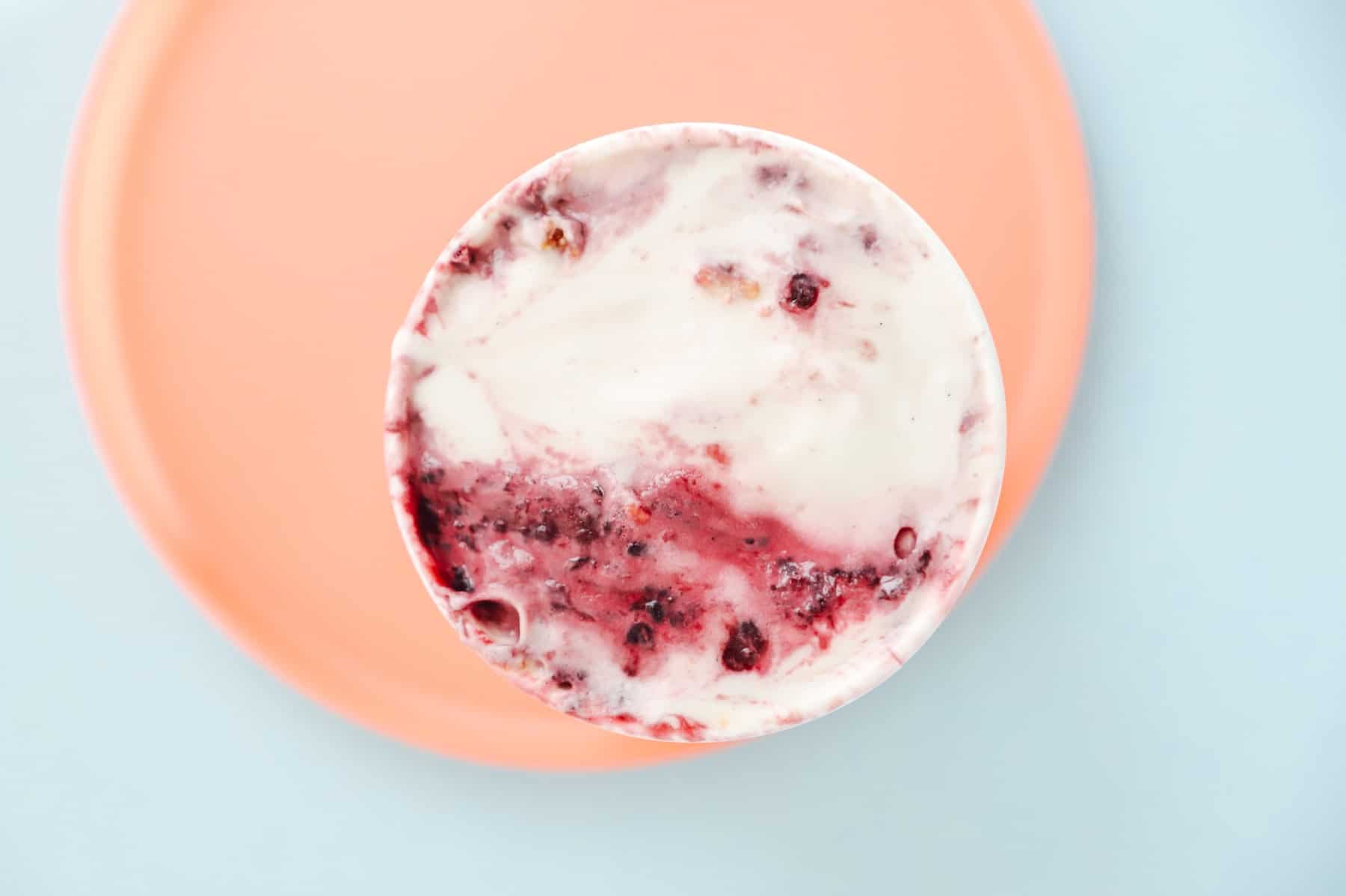 Close up of yogurt with blueberries mixed in on a light blue & pink background