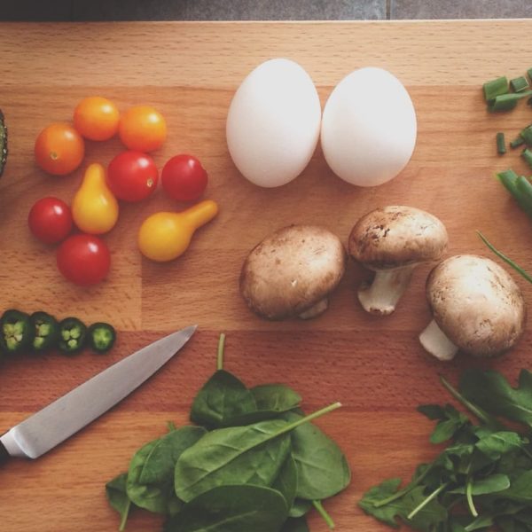wooden cutting board with a variety of healthy fruit including eggs, avocado, basil, and more
