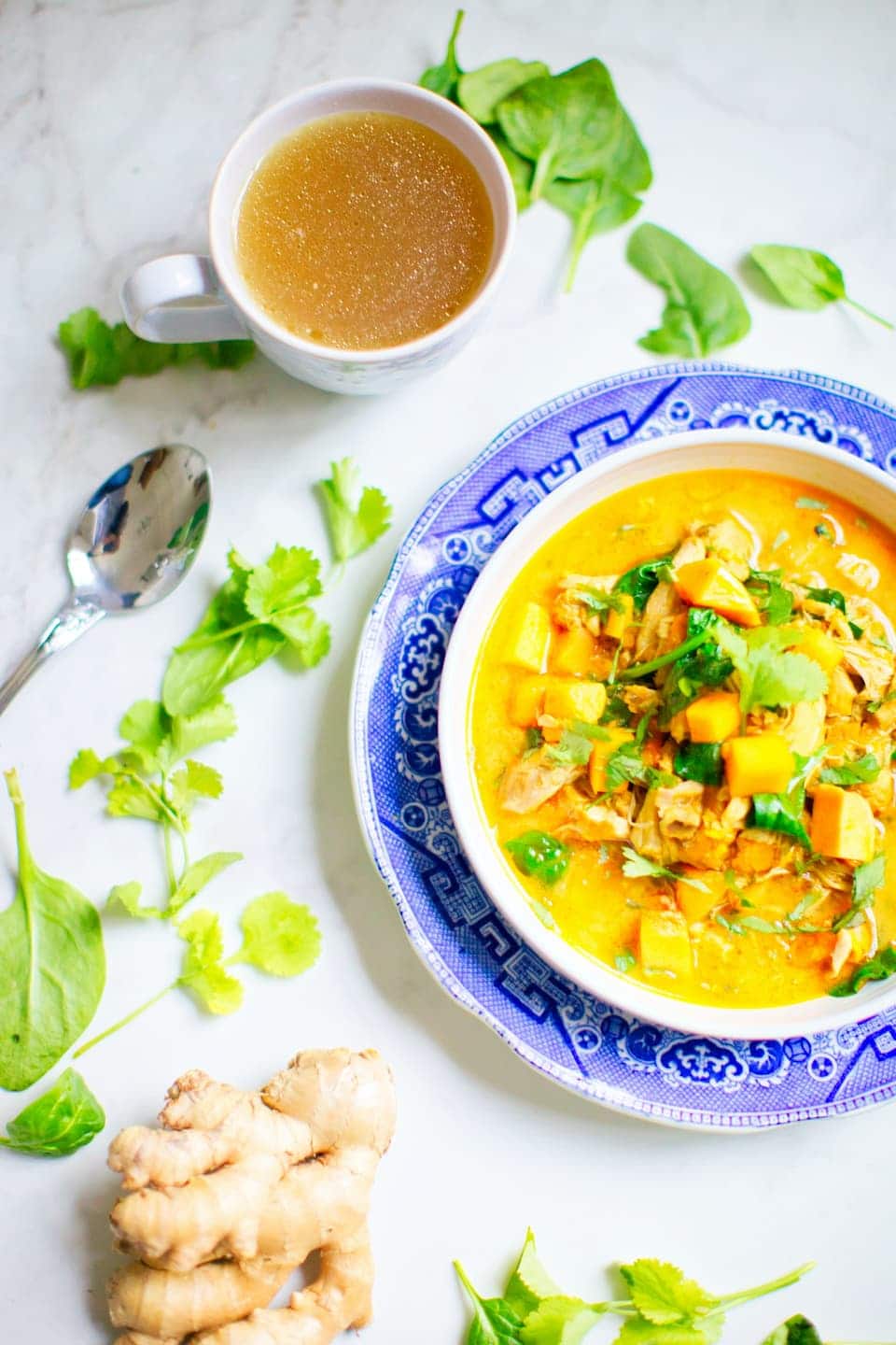 bowl of yellow curry on a blue plate surrounded by ginger and other herbs