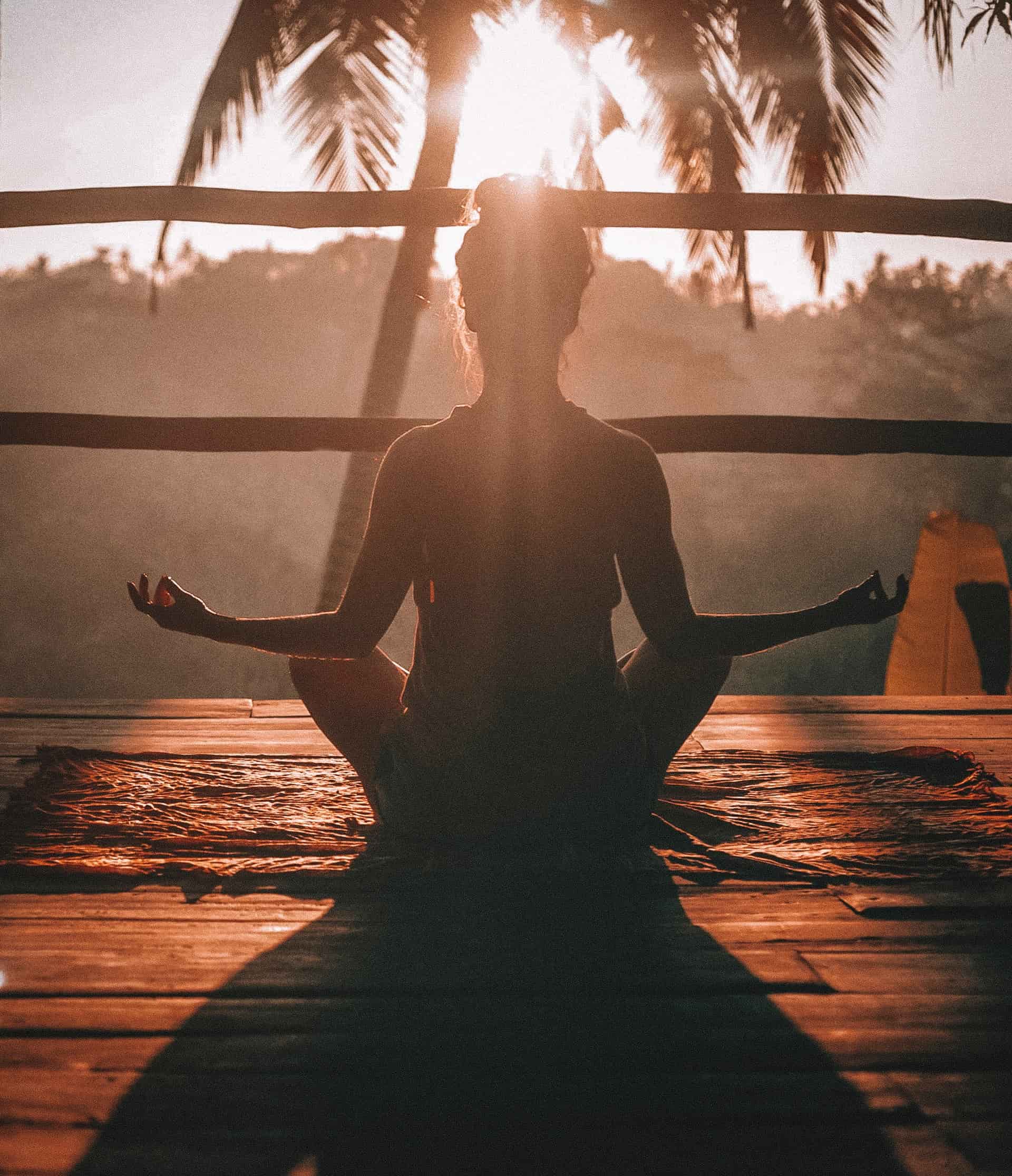 girl doing yoga on a deck with a palm tree and the sunset in the background