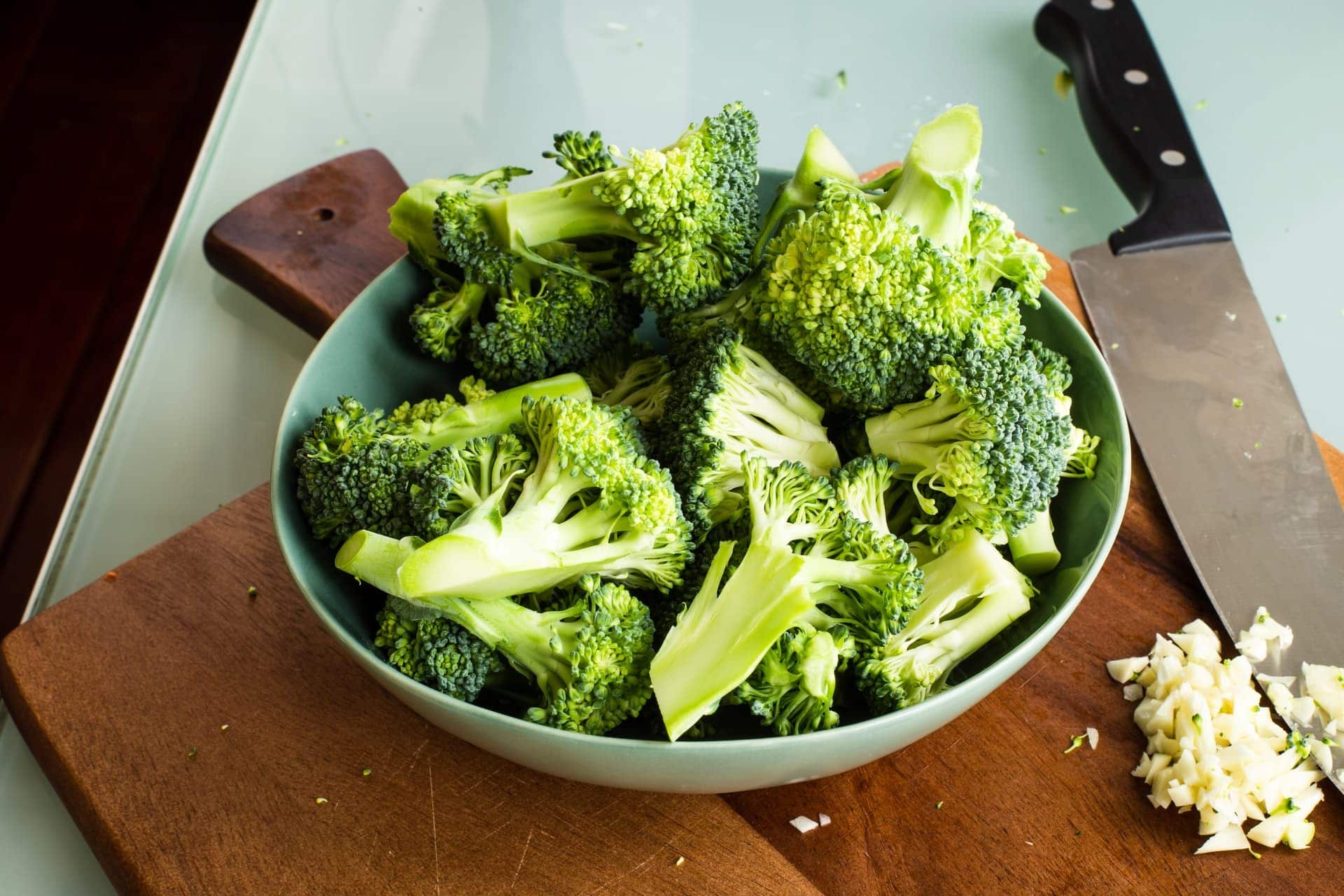 cut-up broccoli in a bowl on a wooden cutting board