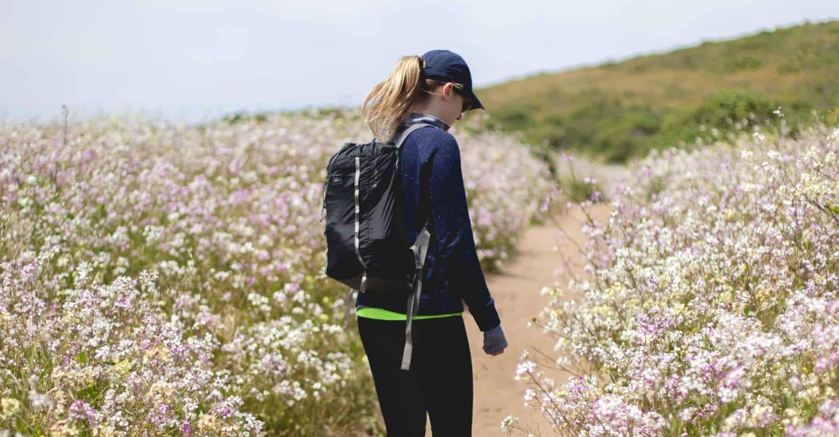 woman walking along a trail with a field of flowers