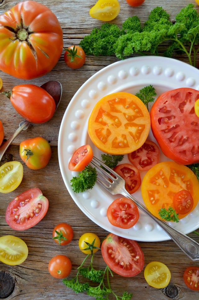 raw, multicolored tomatoes on a white plate